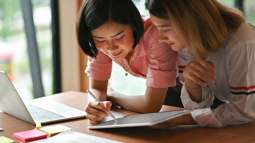 Two female students facing a tablet, working together.