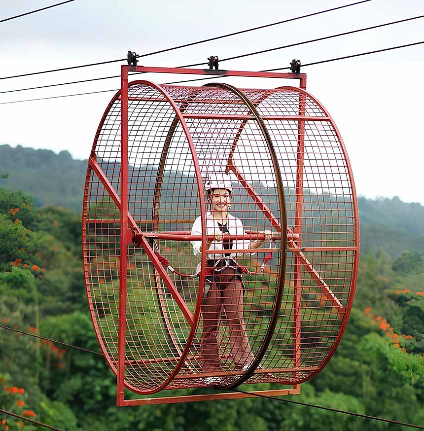 Person inside a suspended red metal cage above a forest.