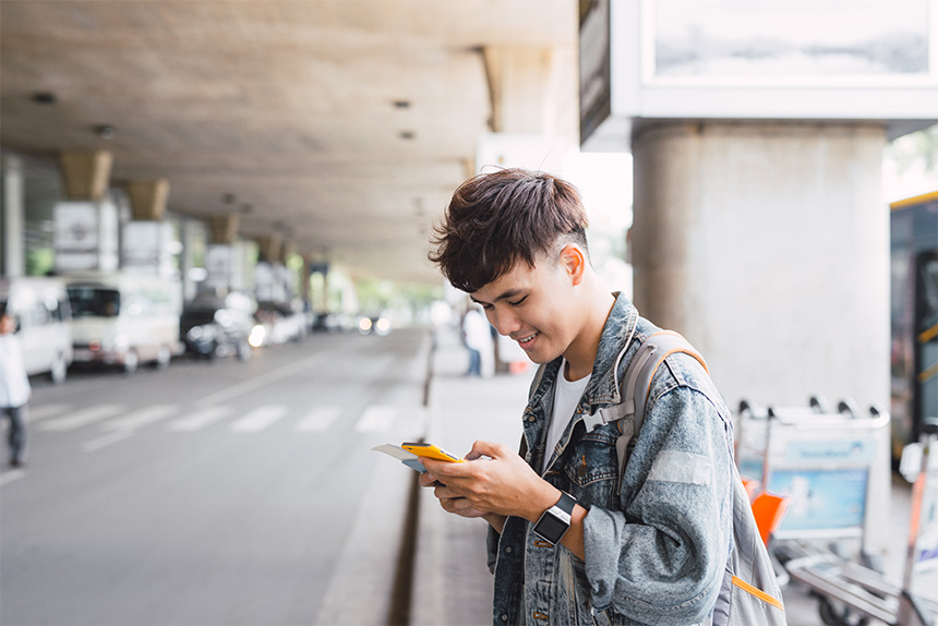 Man using his cellphone while standing on the side of the street.