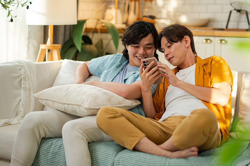 Two men sitting on a sofa at home, watching a video on their phone.