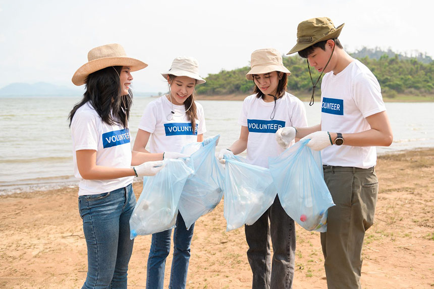 Young Asian men and women holding garbage bags after a beach clean-up initiative.