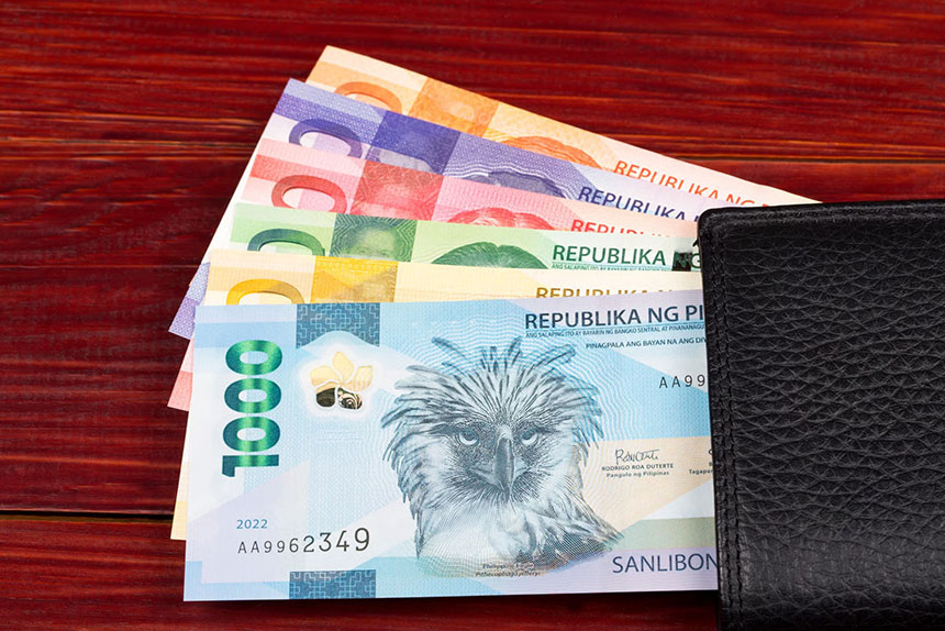 Philippine peso bills in a black leather wallet on a table.