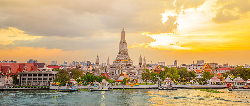 Sunset view of Wat Arun with warm skies and the Chao Phraya River in front.