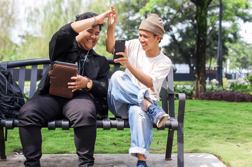 Friends on an outdoor bench celebrating while looking at their gadgets.
