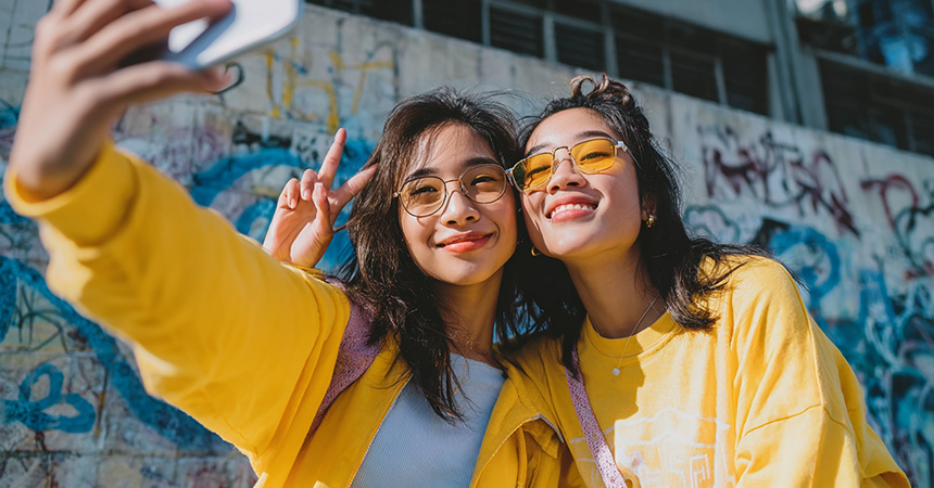 Two girls wearing colorful sunglasses taking a selfie together.