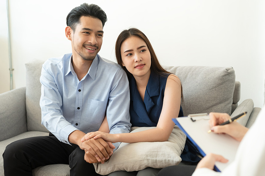Asian couple sitting on a sofa while consulting a doctor at a clinic.