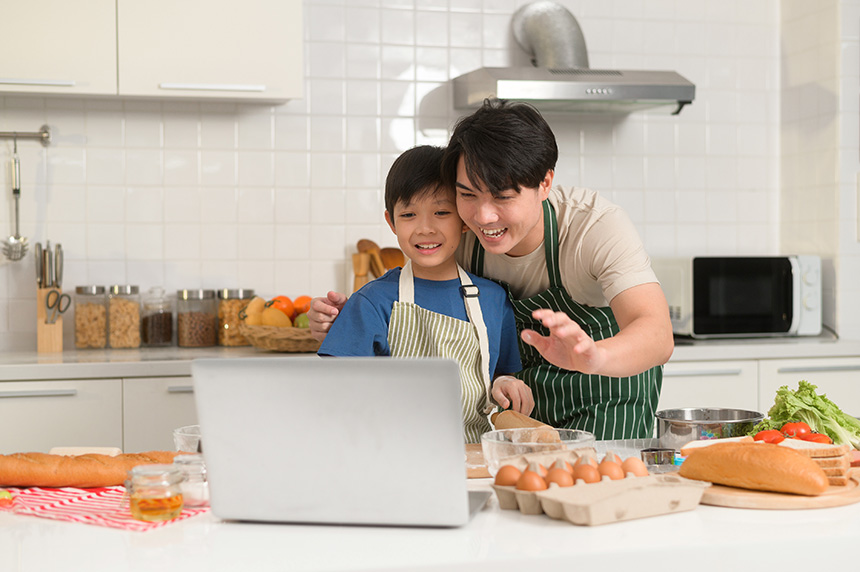 Father and son cooking in the kitchen using a laptop to follow a recipe.