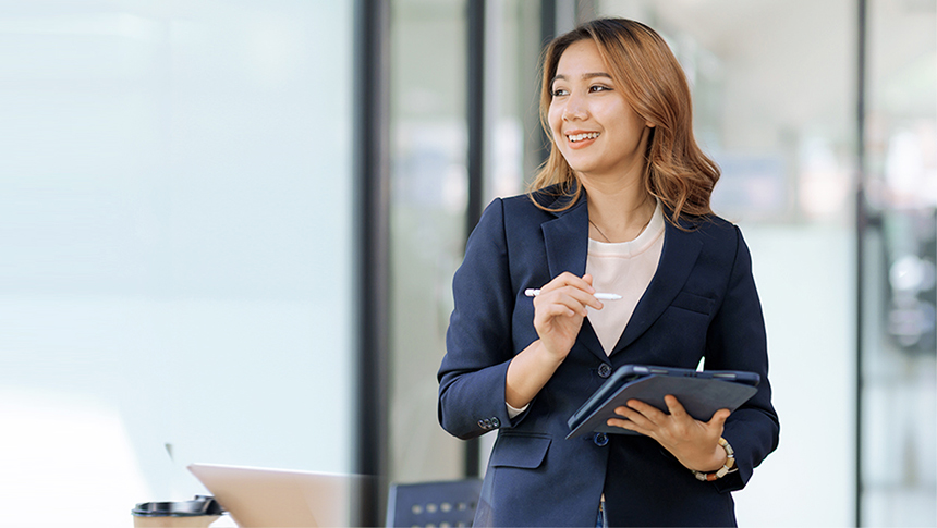 A woman in a professional outfit at the office while holding a tablet.