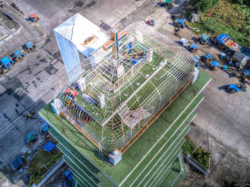 Overhead shot of the Pope John Paul II Tower featuring a prominent cross on its roof, surrounded by greenery and other structures.