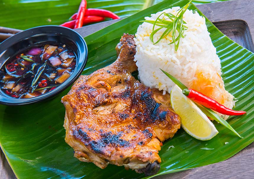Plate of Bacolod chicken inasal with garlic rice, lemon, and spiced vinegar dipping sauce on a banana leaf.