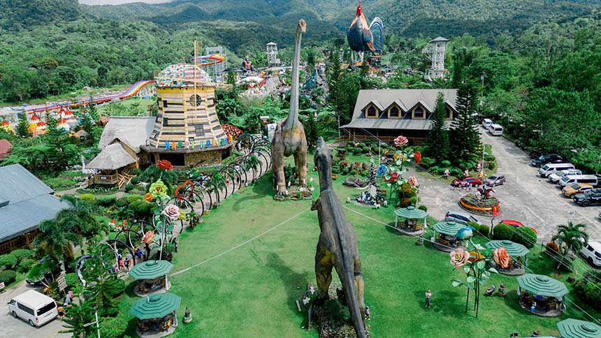 Aerial view of Campuestohan Highland Resort in Negros Occidental featuring dinosaur statues, colorful rides, and mountain scenery.
