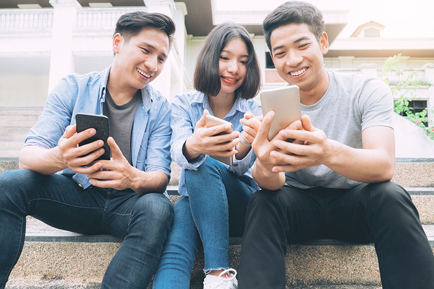 Three young Asian friends using and looking at their devices together.