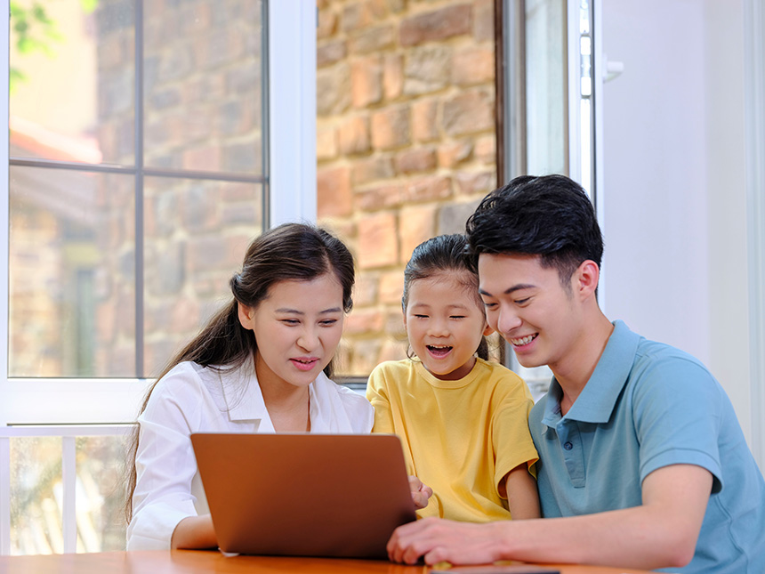 Family smiling together while looking at a laptop at home, planning a trip or activity.