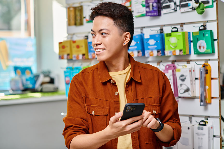 Young Asian man holding his smartphone and looking away in store.