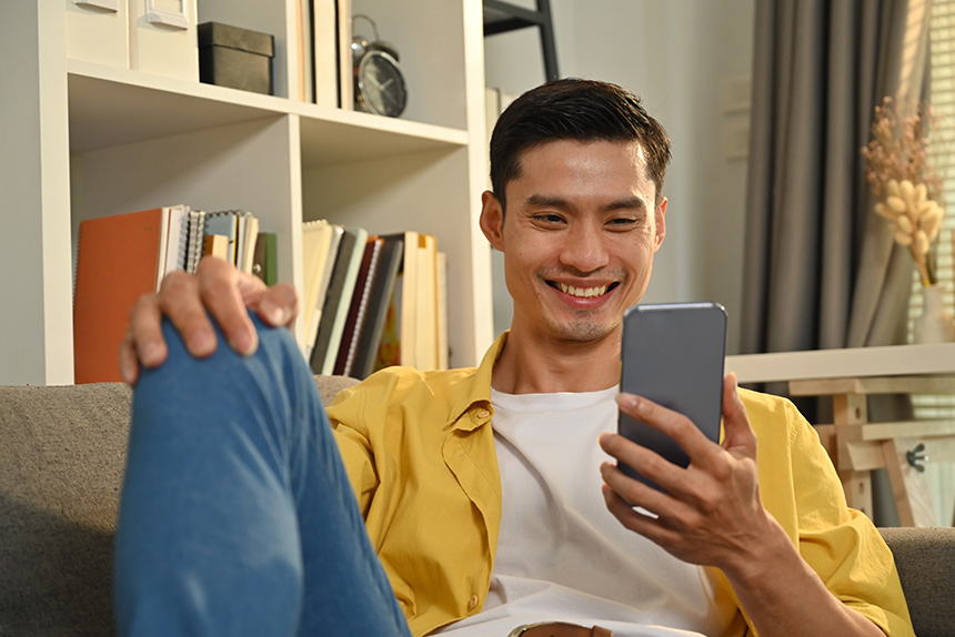 Young Asian man relaxing on couch at home while looking at social media.