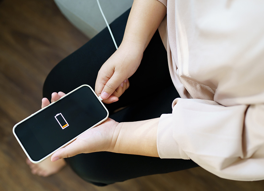 Top shot of a womanâs hands holding a low-batt smartphone and charging cable.