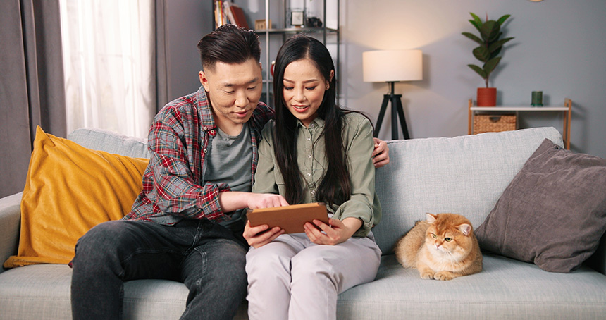 Couple relaxing on a sofa with their dog, using a smartphone while enjoying time together at home.