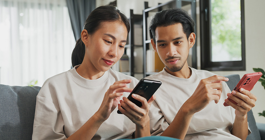 An Asian couple on their smartphones at home, learning how to manage their Globe prepaid eSIM.