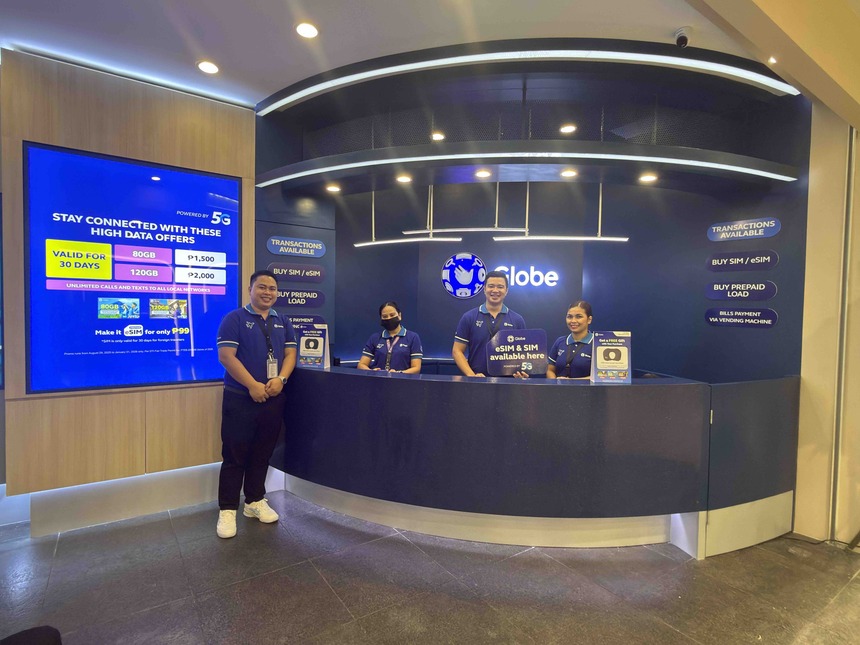 Four Globe staff members standing behind a blue service counter at the new NAIA Terminal 3 arrival store.