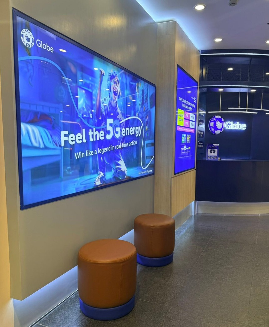 Interior of the Globe NAIA store featuring brown seating stools and a large "Feel the 5G energy" digital poster.
