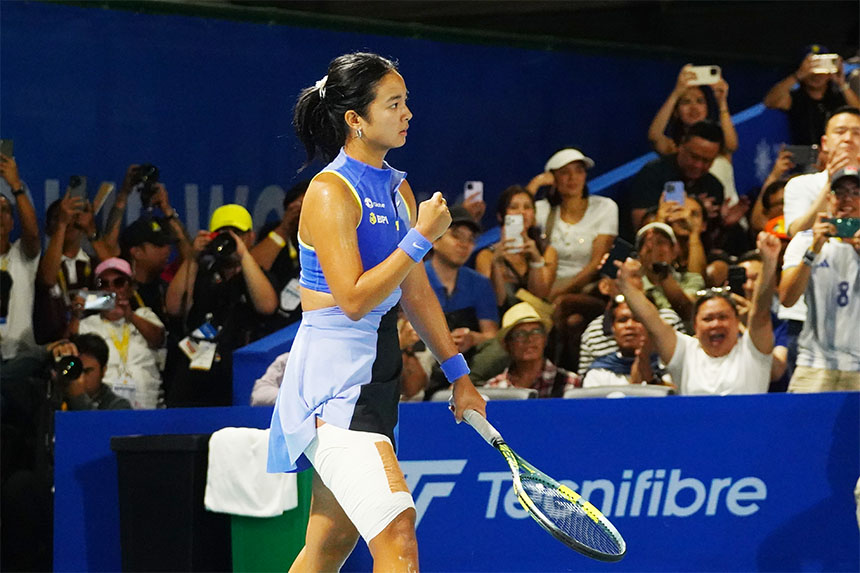 Alex Eala in a blue and white tennis outfit stands with a racket, poised for action on the court.