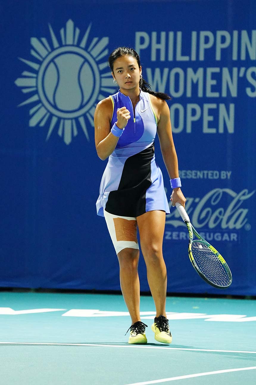 Alex Eala in a blue and black dress holds a tennis racket, ready to play.