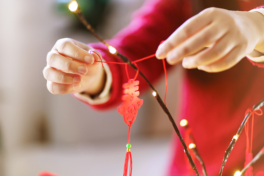 Close-up of an Asian woman placing a red Chinese New Year good luck pendant on a decorated branch.