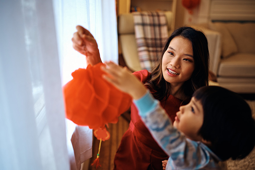 Mother and child hanging a red lantern by the window as they prepare for Chinese New Year.