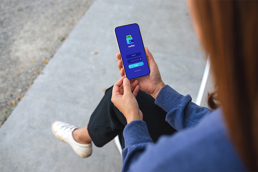 Photo of a woman sitting outside holding her smartphone as she logs in on an app.