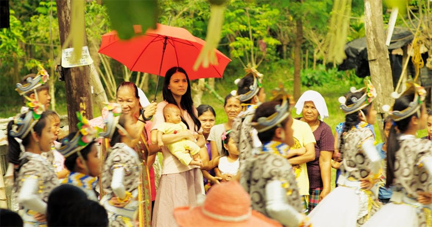 A woman cradles a baby while surrounded by a cheerful group of Bambanti Festival street dancers.