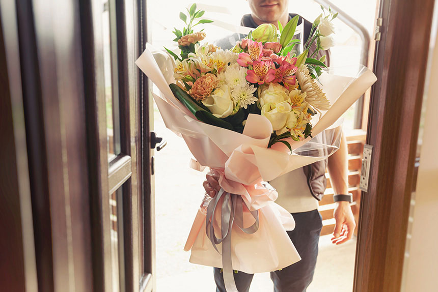 Male messenger delivers a bouquet of flowers at a house.
