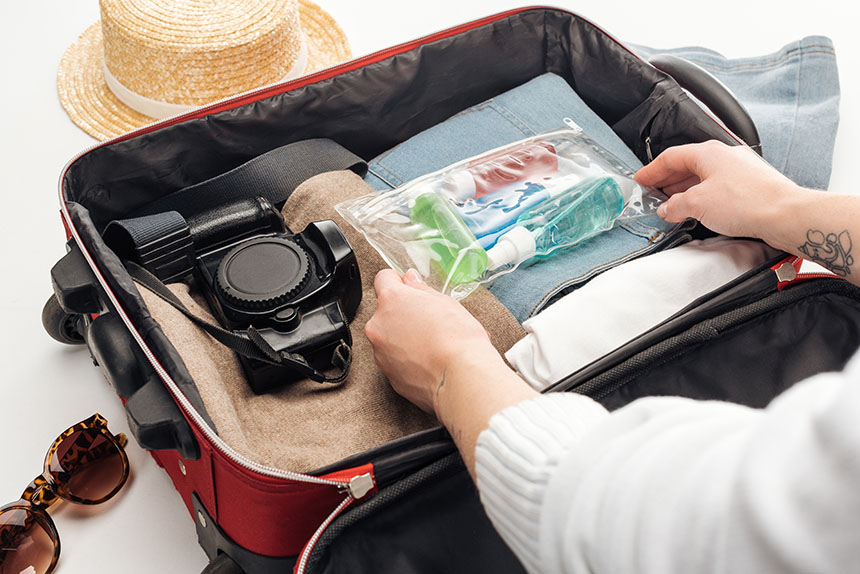 Traveler placing travel-size liquids in a clear pouch while packing a suitcase