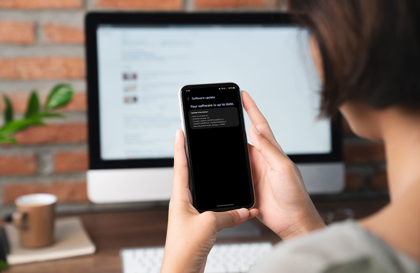 A woman multitasks, checking her email on her computer and glancing at her phone.