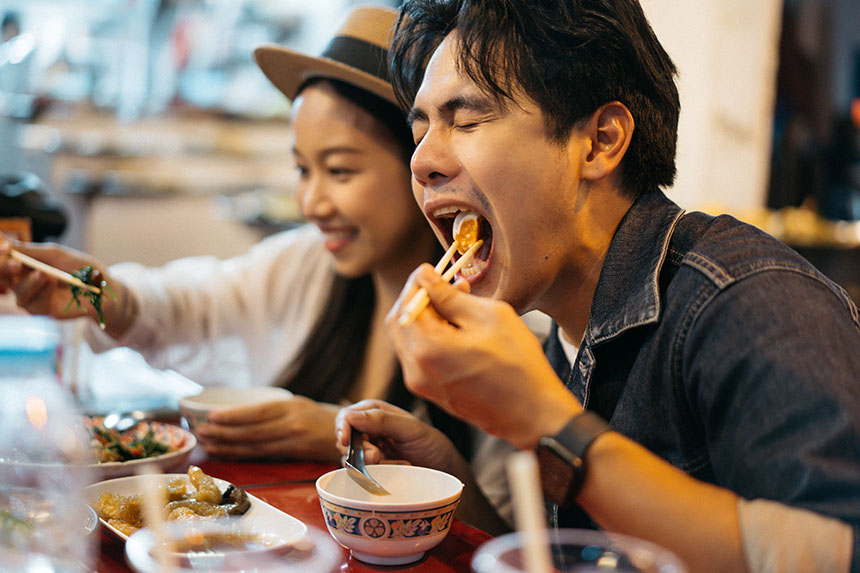 A young couple happily dining at a restaurant, surrounded by plates of delicious Chinese food.