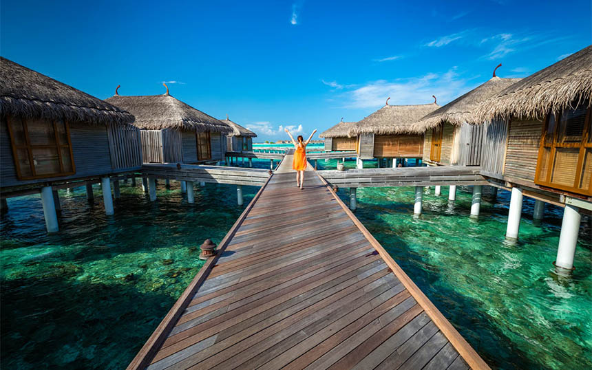 Female traveler walks along water bungalows in the Maldives.