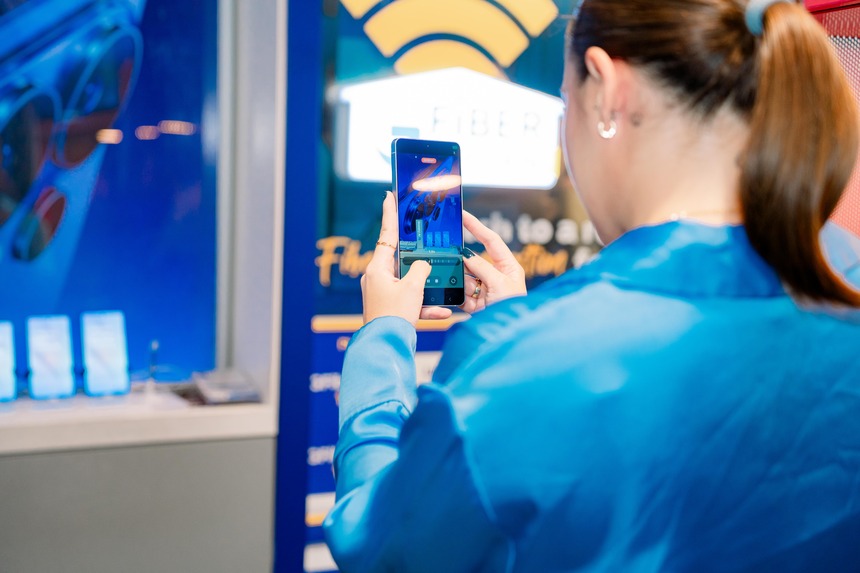 A woman uses a smartphone to take a photo of the Samsung Galaxy S26 display.