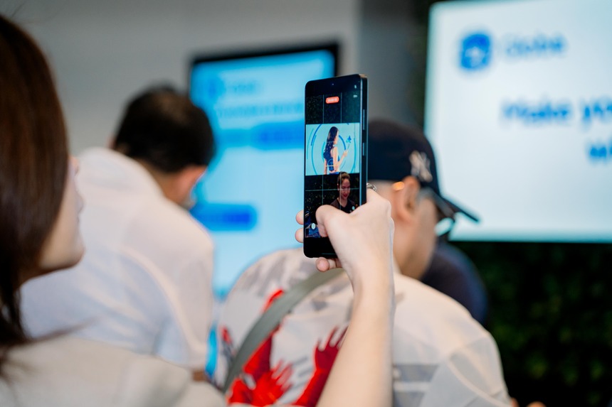 A woman uses a smartphone to record a live presentation during an event.