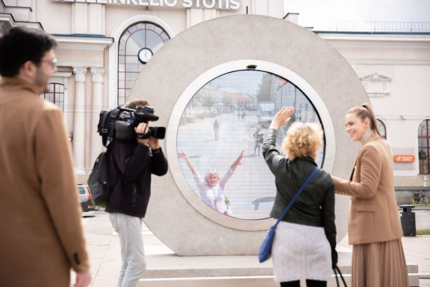 People gathering on a city street facing a circular Portal installation displaying a live video feed from another city.
