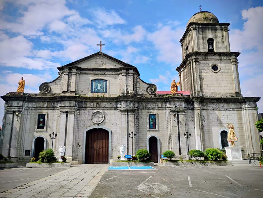 Exterior view of Imus Cathedral featuring its historic stone facade, central entrance, and bell tower beneath a partly cloudy blue sky.