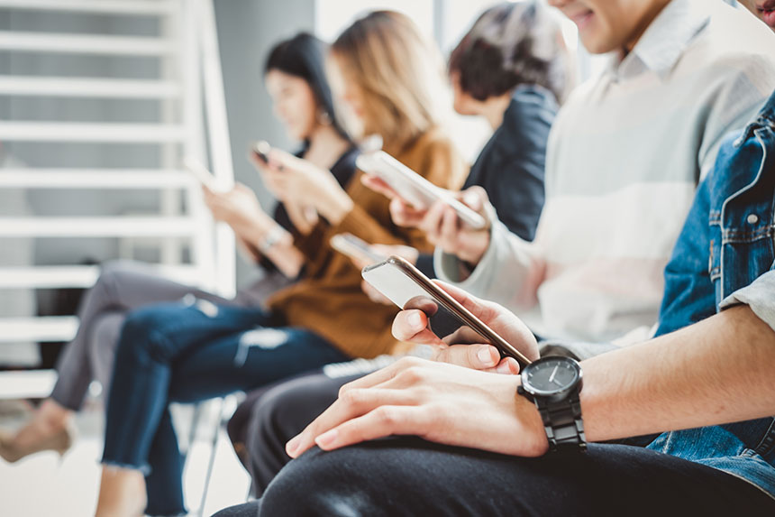 A group of people sitting in a row, each using a smartphone.