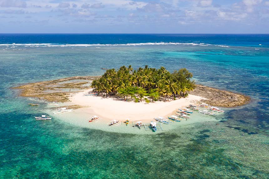 Aerial view of a tropical island with white sand, palm trees, and boats in Siargao.