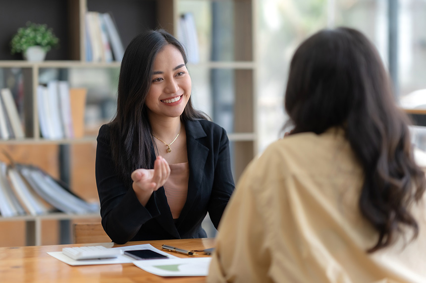 Two Filipino businesswomen talking and collaborating in an office, engaged in a discussion.