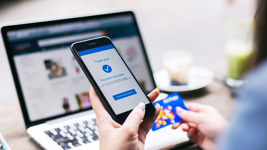 A woman making a successful online payment on a smartphone while holding a card.