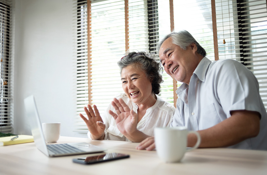 Elderly couple smiling and waving during a video call at home.