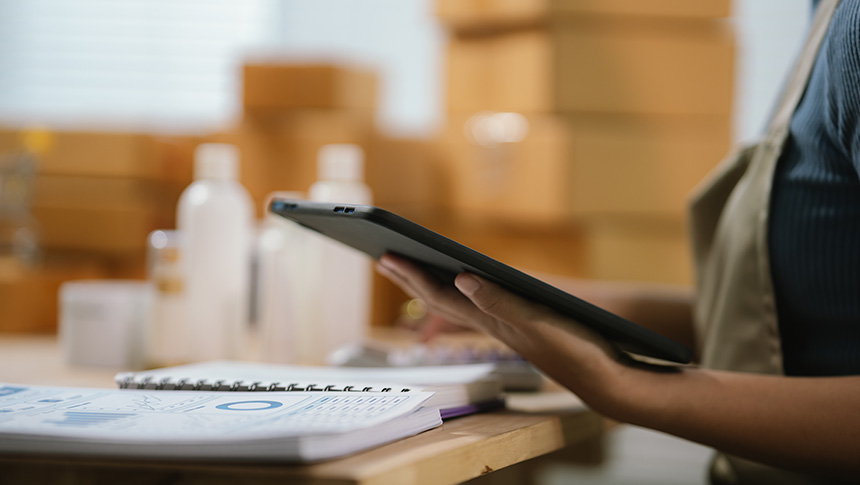 A person reviewing financial documents on a tablet beside bookkeeping papers on a desk.