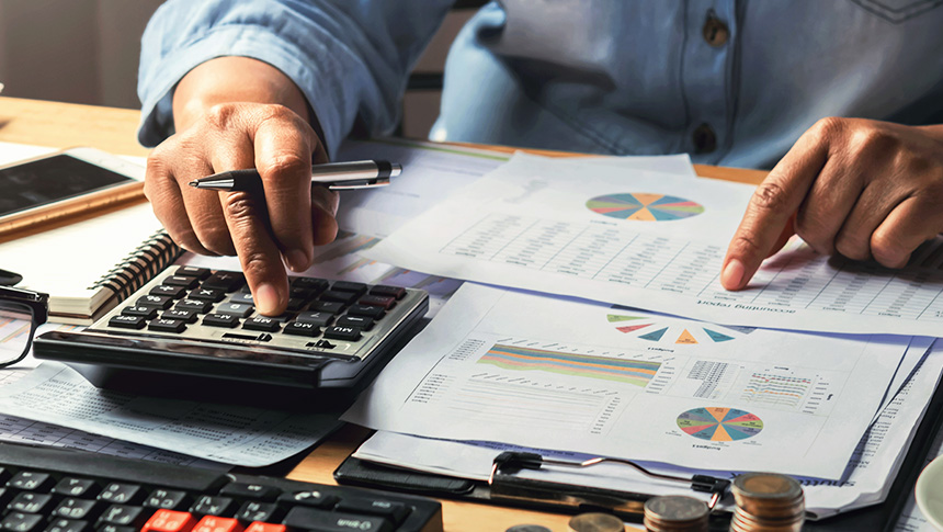A person using a calculator while reviewing printed financial charts and documents on a desk.