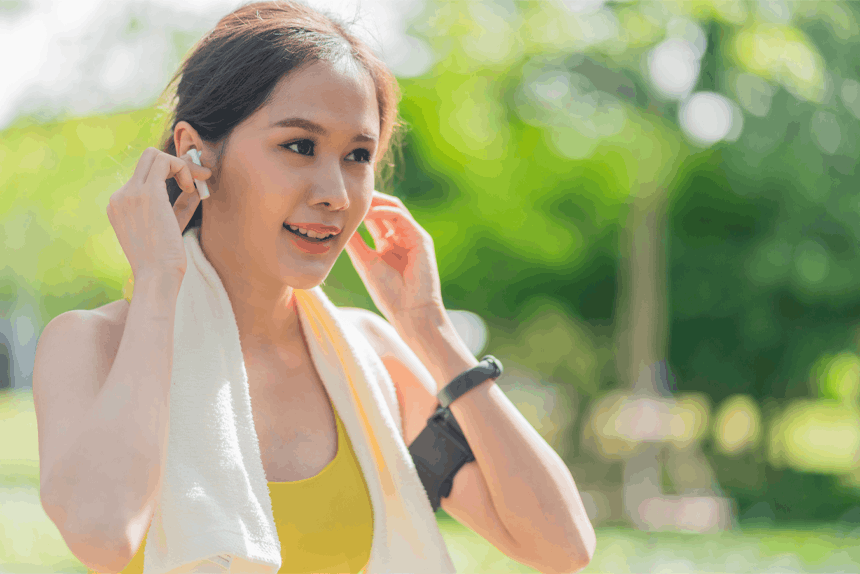 A woman adjusts her earbuds after a workout in a sunny, lush green park, with soft natural lighting.
