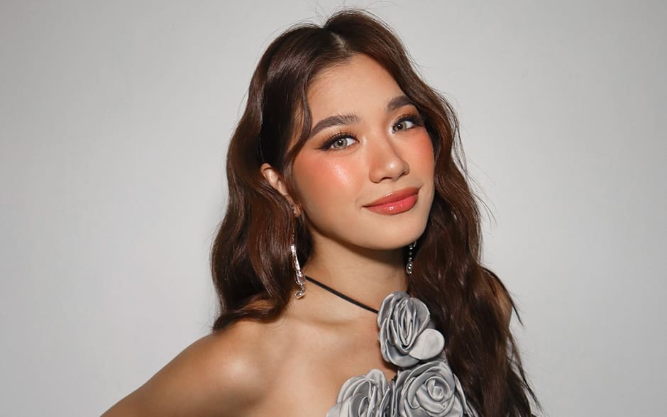 BINI Aiah posing confidently in a floral-themed gray top and a red skirt with delicate embellishments, against a plain white background.