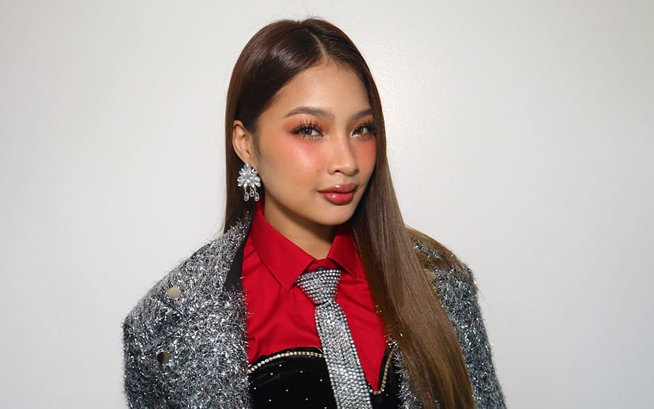 BINI Colet in a silver jacket, red shirt, and sparkling tie, posing against a white background..