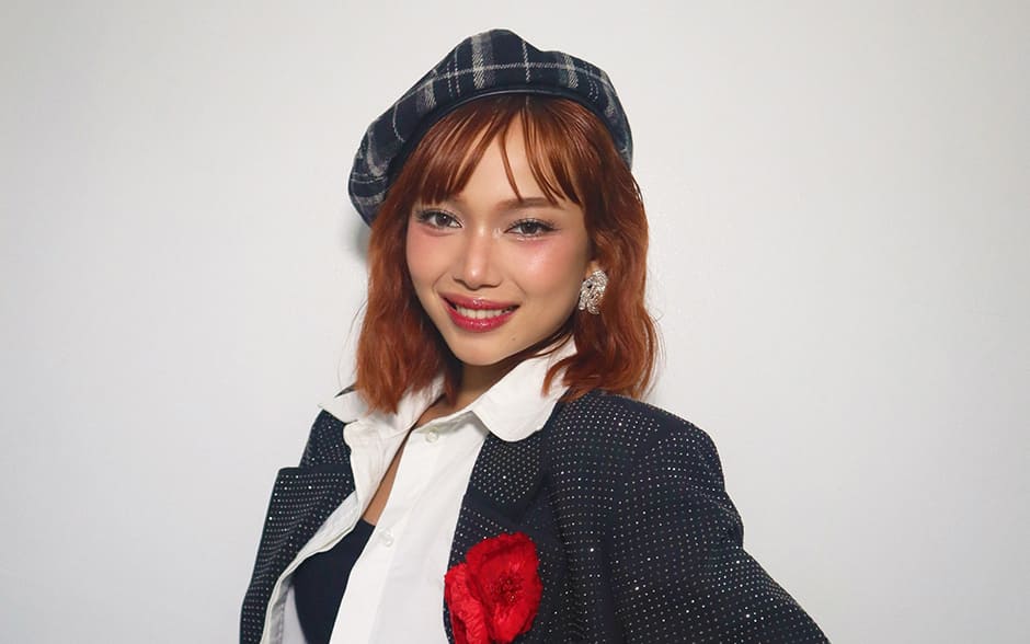 BINI Gwen posing gracefully in a stylish outfit featuring a plaid beret, a glittering blazer with a red flower accent, and a shimmering belt.